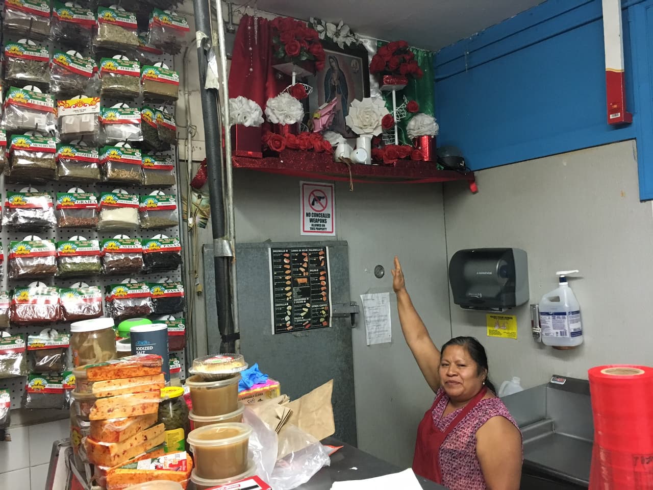 Una mujer señala un altar de la Virgen de Guadalupe en una carnicería en Boyle Heights que -según su propietario- no ha sufrido robos violentos.