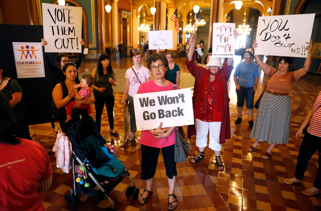 <b>"No estamos dispuestas a retroceder"</b>, dice el mensaje de esta mujer durante una protesta en las afueras de la oficina de la gobernadora Reynolds para pedirle que vetara el proyecto de ley que prohíbe los abortos después de las seis semanas de embarazo. También se observa un gancho de ropa, usado para abortar de forma clandestina cuando es posible acceder a un procedimiento seguro. "No les pertenecemos", se lee en otra pancarta.