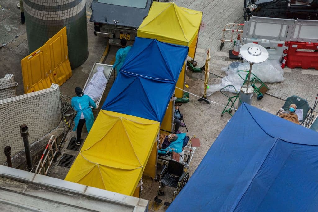 Otro de los servicios que ha llegado al tope es el funerario y las morgues. En la imagen, trabajadores de una funeraria mueven el cuerpo de un fallecido por covid-19 hacia un vehículo. En el mismo espacio, se ven pacientes que reciben atención fuera del centro médico Caritas.