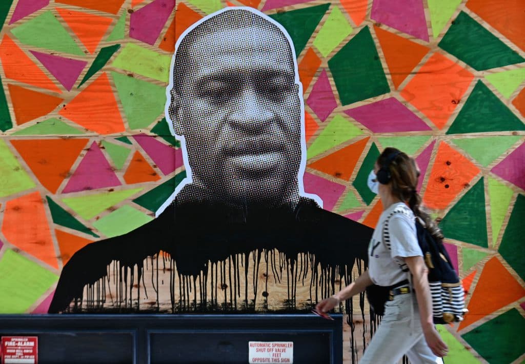 A woman walks past a boarded up store front with a George Floyd mural on June 10, 2020 in New York City.