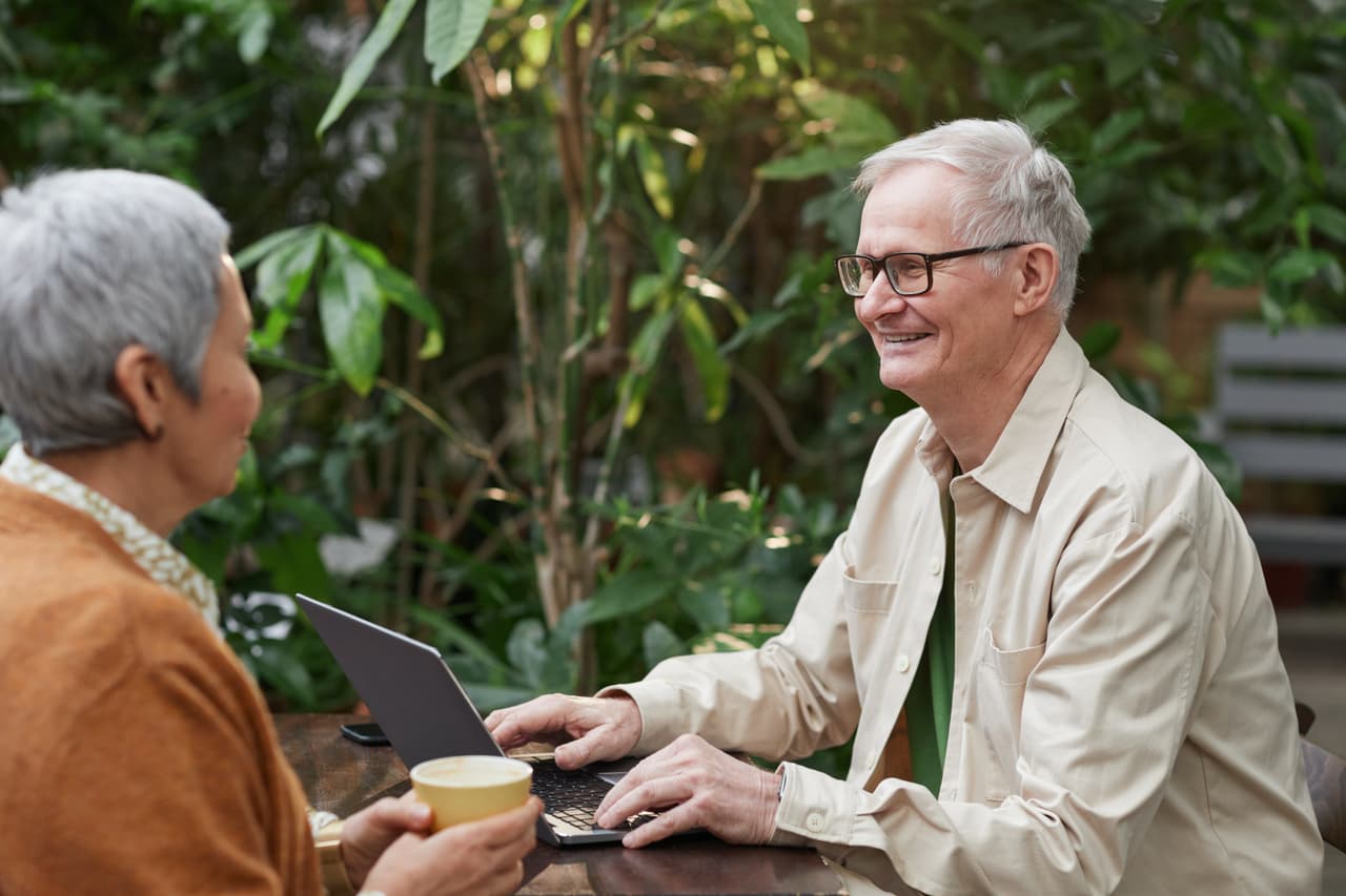 A man on a computer smiles and looks at a woman next to him.