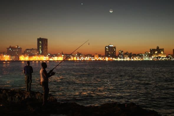 Un grupo de hombres se reúne al atardecer para pescar a lo largo del Malecón frente al mar en La Habana.