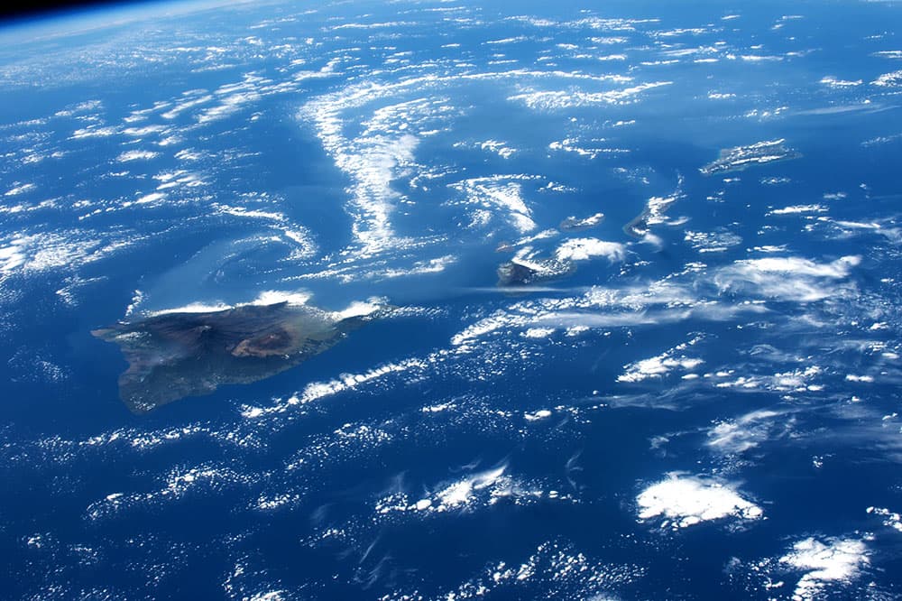 Los expertos a bordo de la EEI orientaron la cámara específicamente para capturar este panorama del volcán Kilauea de Hawai (a la izquierda) con los largos remolinos de gases volcánicos (la mitad superior de la imagen) flotando hacia el oeste desde el volcán. Los astronautas están entrenados para tomar imágenes oblicuas de neblina atmosférica difícil de ver al disparar oblicuamente para mejorar la visibilidad.