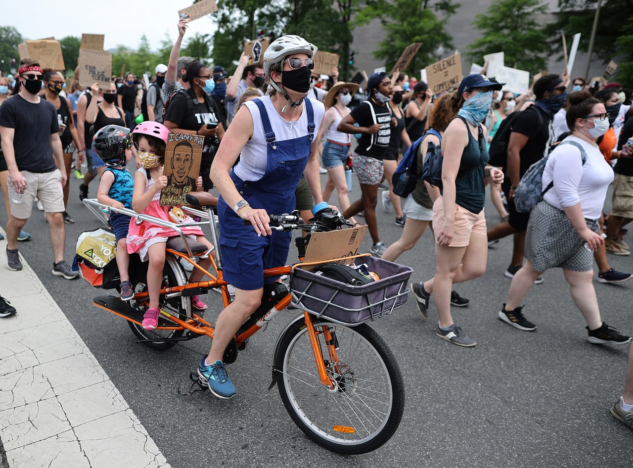 Una mujer lleva va en bicicleta con dos niños durante la masiva manifestación en Washington DC. El Servicio Secreto desplegó nuevas barreras de protección en el perímetro de la mansión presidencial, pero esta manifestación se ha extendido a varias calles del centro de la ciudad.