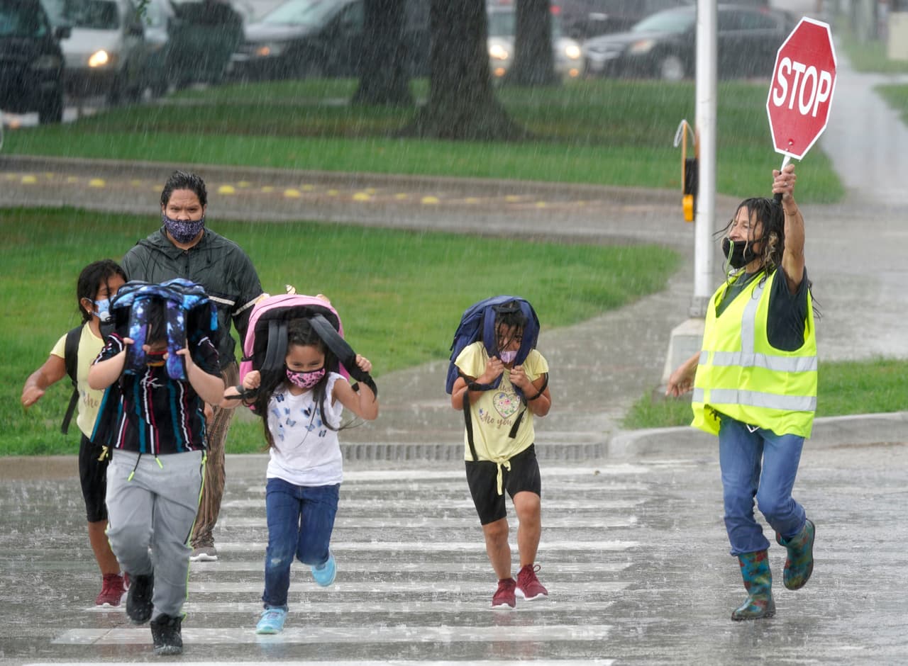 Un guardia de cruce detiene el tráfico para que los niños de la escuela primaria crucen la calle durante una tormenta en Richardson, Texas, tras reanudar las clases presenciales.