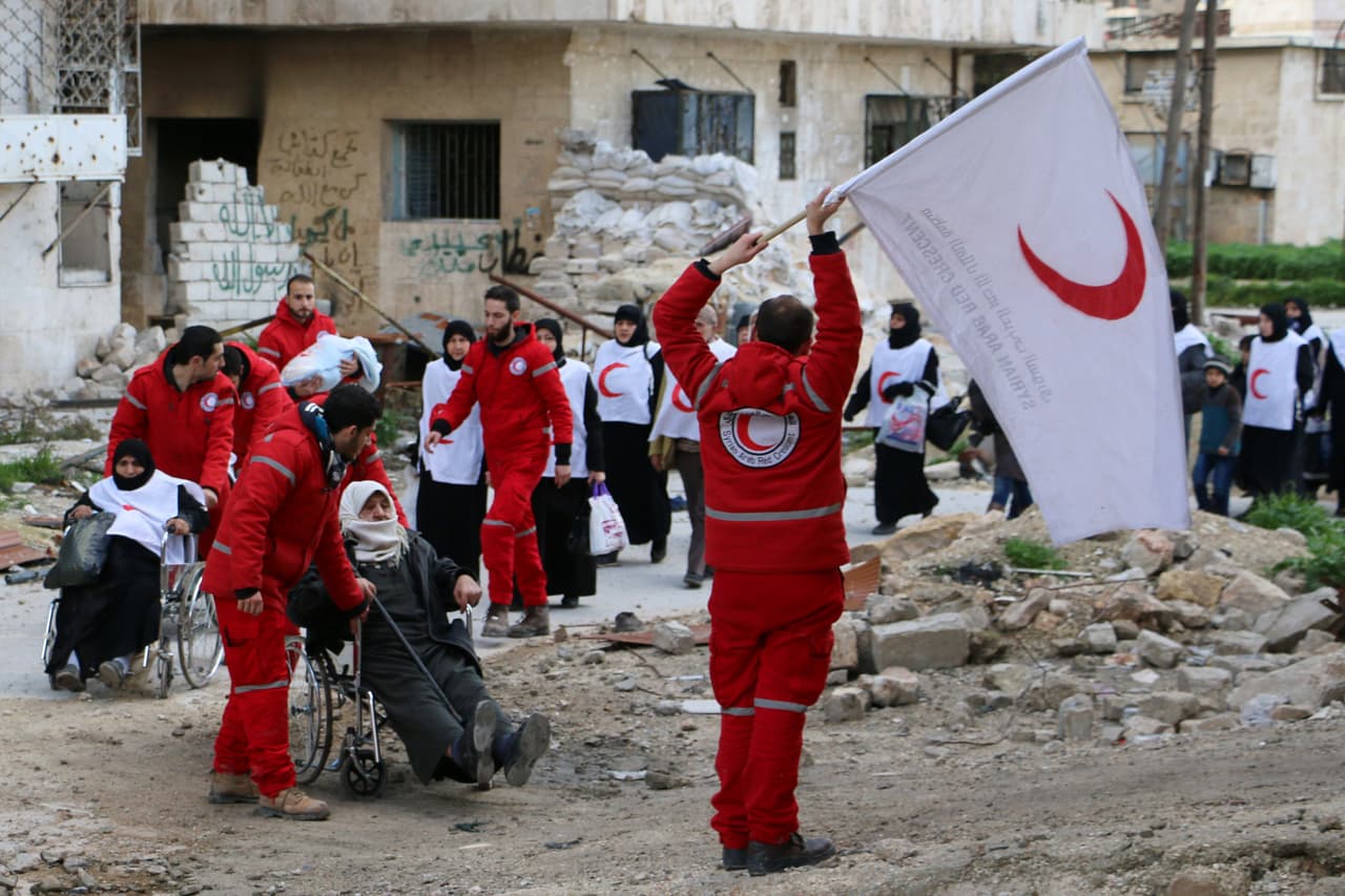 Miembros de la Media Luna Roja (versión musulmana de la Cruz Roja Internacional) guían a los civiles sirios desde una zona controlada por los rebeldes a otra controlada por el gobierno en el distrito de Bustan al-Qasr.