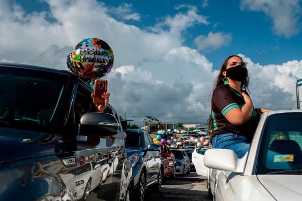 Una graduanda de la Escuela Secundaria Ramón Power y Giralt en Puerto Rico sale por la ventana del auto con un tapabocas.