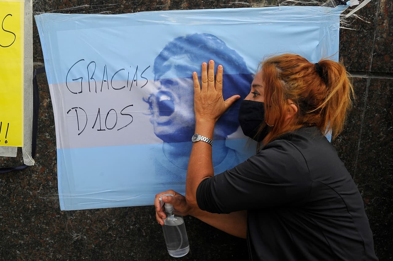 Una fan de Maradona acaricia una bandera con el rostro del exjugador colgada en una pared de Buenos Aires días después de la cirugía en la cabeza, a la que fue sometido recientemente tras hallarle un hematoma.