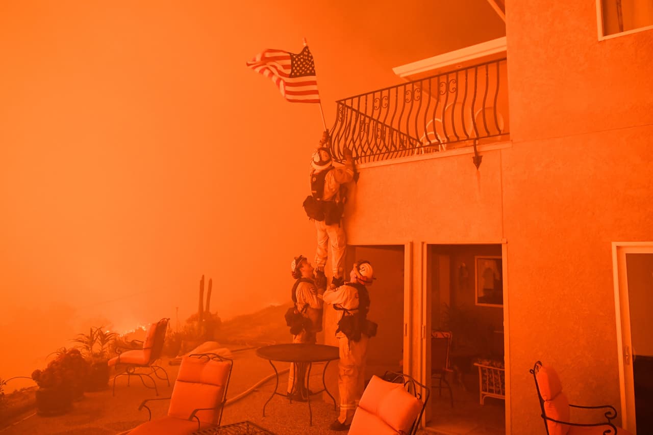 <b>California en llamas.</b> Imparables incendios azotaron territorios del norte y sur de California a lo largo del año, 
<b><a href="https://www.univision.com/los-angeles/kmex/noticias/incendios/el-incendio-thomas-no-se-detiene-y-se-convierte-en-el-segundo-mas-grande-en-la-historia-de-california">causando devastación y destrozos materiales</a></b>. Desde los viñedos del noroeste de San Francisco, hasta los suburbios de mansiones multimillonarias en Los Ángeles, muchos perdieron sus propiedades con las llamas. En la fotografía, bomberos de Oroville quitan una bandera de EEUU izada en una casa a la que se le acercan las llamas impulsadas por el viento. 8 de julio de 2017.