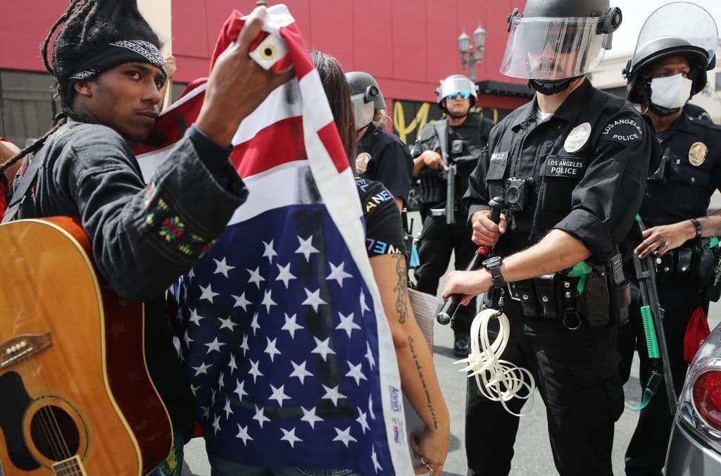 Este manifestante sostiene la bandera de EEUU al revés mientras confronta a la policía durante una manifestación pacífica por
<a href="https://www.univision.com/noticias/estados-unidos/asesinaron-a-mi-hermano-estaba-pidiendo-ayuda-familiares-de-george-floyd-claman-justicia">la muerte de George Floyd</a> en Hollywood, en Los Ángeles, California. Las multitudinarias protestas contra el racismo y la violencia policial tras la muerte de George Floyd, un hombre negro a manos de la Policía de Minnesota se intensificaron el martes hasta entrada la madrugada del miércoles en diversos puntos del país.