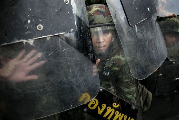 Militares tailandeses están detrás de sus escudos antidisturbios mientras los manifestantes les amenazan.