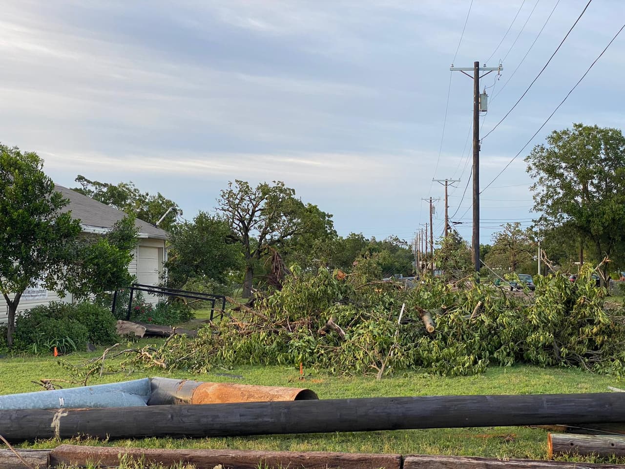 Montaña de hojas y ramas acumuladas frente a una residencia afectada.