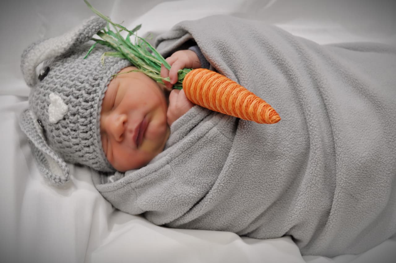 Este bebé, en Frisco, luce un gorro tejido con orejas de conejo de pascua y está muy envuelto en su manta.