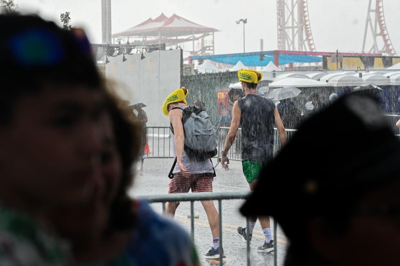 Los fans con sus sombreros de perritos calientes de Nathan se van después de que una tormenta pospuso la competencia por horas.