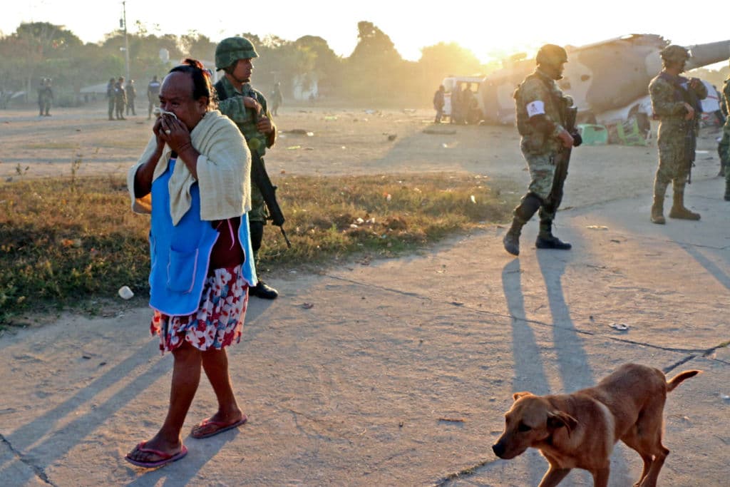 Una mujer de la comunidad de Santiago Jamiltepec, Oaxaca, pasa junto a los soldados que hacen guardia en la zona del accidente en que el helicóptero militar cayó sobre varios vehículos con gente que pasaba allí la noche luego de que sus viviendas sufrieran daños por un sismo ocurrido en la tarde del viernes.