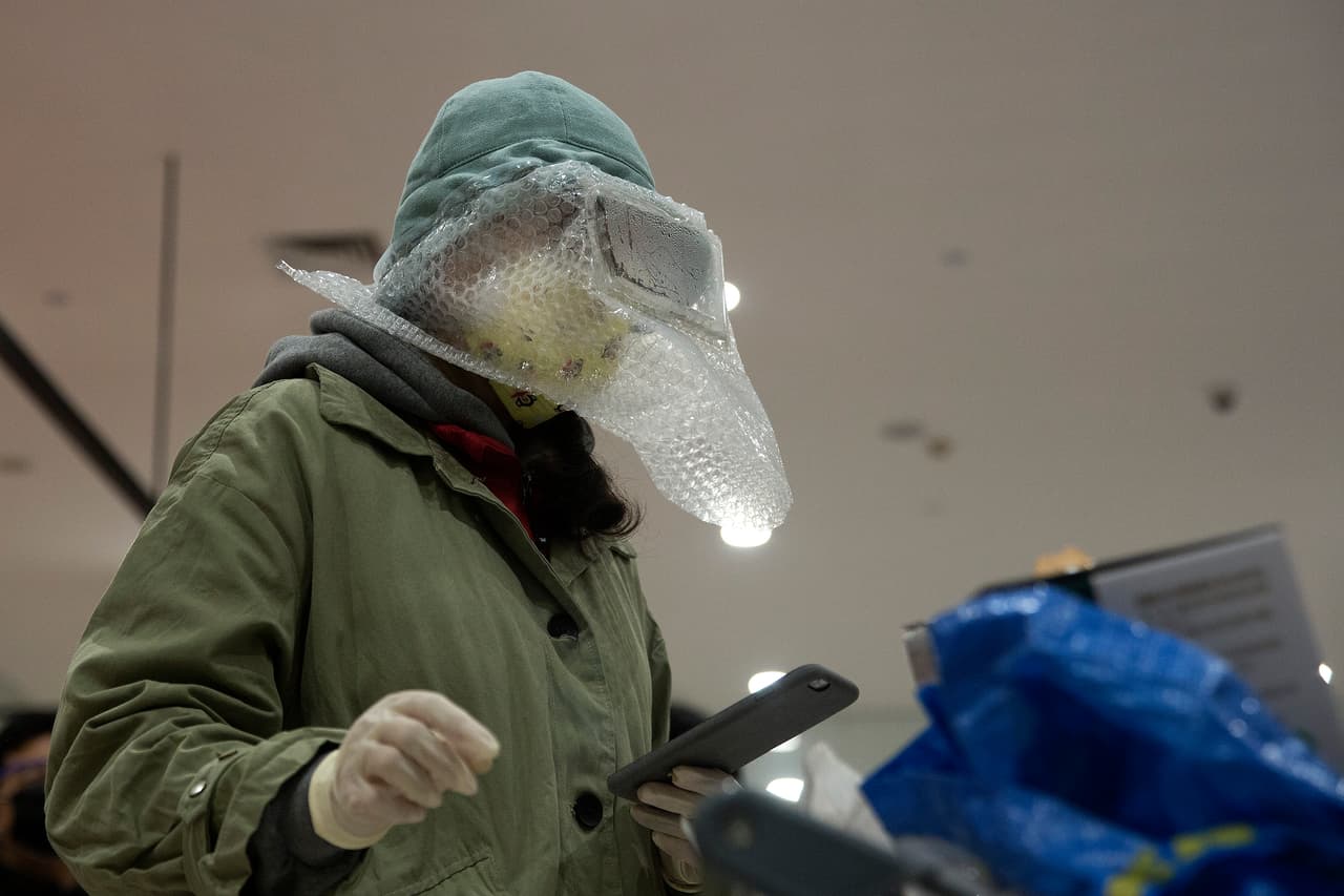 En la foto se ve a una mujer en el supermercado en Wuhan, cubierta con máscara, un folio plástico y guantes en las manos. Mucha gente ni siquiera sale de sus casas.