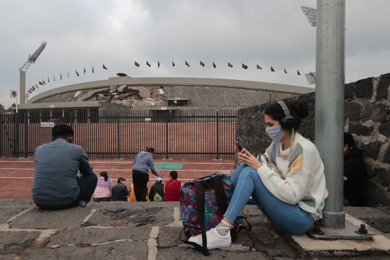 Una persona mira su teléfono celular afuera del estadio mientras espera a un familiar que toma el examen de admisión. 
<br>
<br>A pesar de que algunas escuelas de México están experimentando con realizar las pruebas por videoconferencia, donde los docentes pueden observar a los aspirantes para asegurarse de que no hagan trampa, 
<b>es tanta la importancia del examen de ingreso a la UNAM, y la preocupación en torno a escándalos anteriores sobre supuestas trampas o preguntas filtradas, que la universidad hizo que los estudiantes se presentaran en persona.</b>
<br>