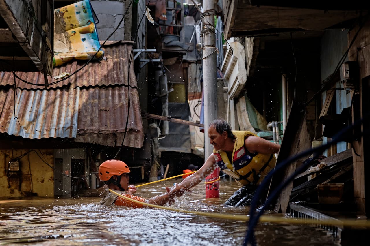 Un trabajador de emergencias ayuda a un colega en las labores de rescate en un barrio inundado en Yakarta.