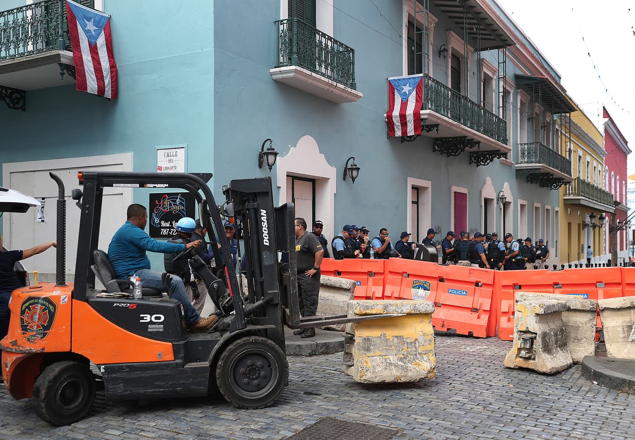 La policía reubica las barricadas de cemento a lo largo de una calle cerca de la mansión del Gobernador mientras se preparan para las protestas programadas para hoy,