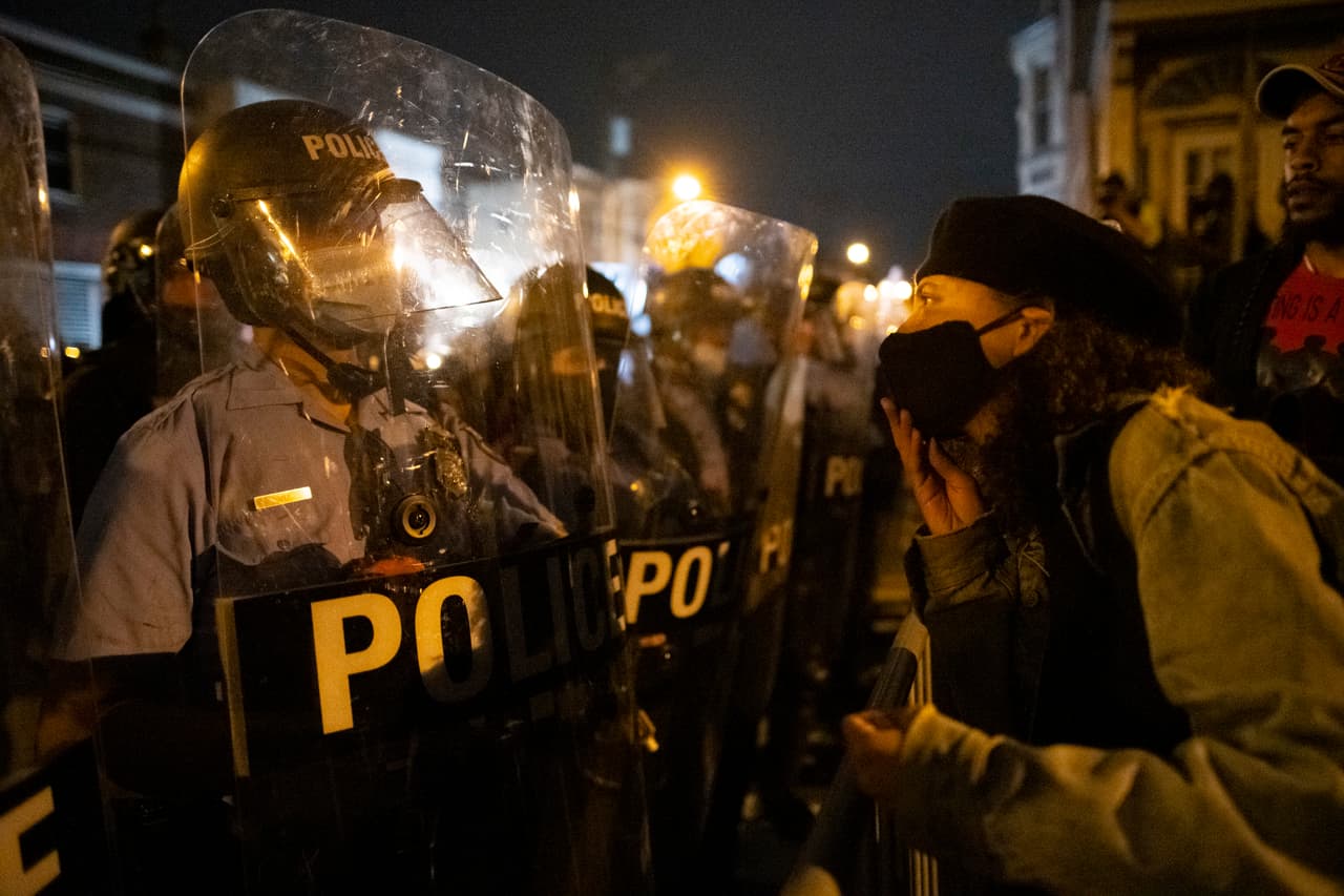 Un manifestante se enfrenta a los oficiales de policía que forman una línea de barricada durante una protesta que inició de forma pacífica.