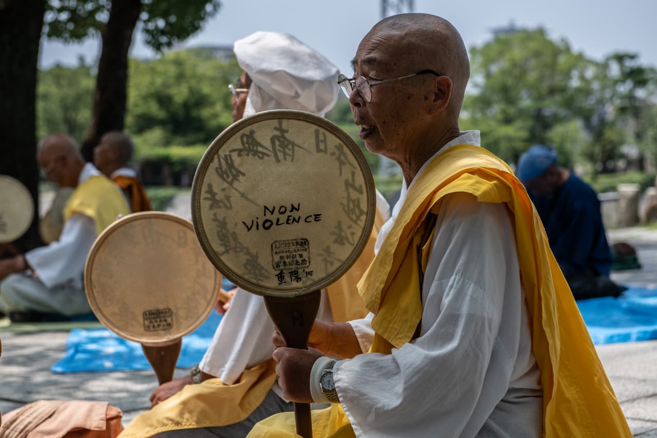 Un monje golpea un tambor
<b>donde se puede leer la frase "sin violencia" escrita en él, mientras reza junto a la Cúpula de la Bomba Atómica.</b>