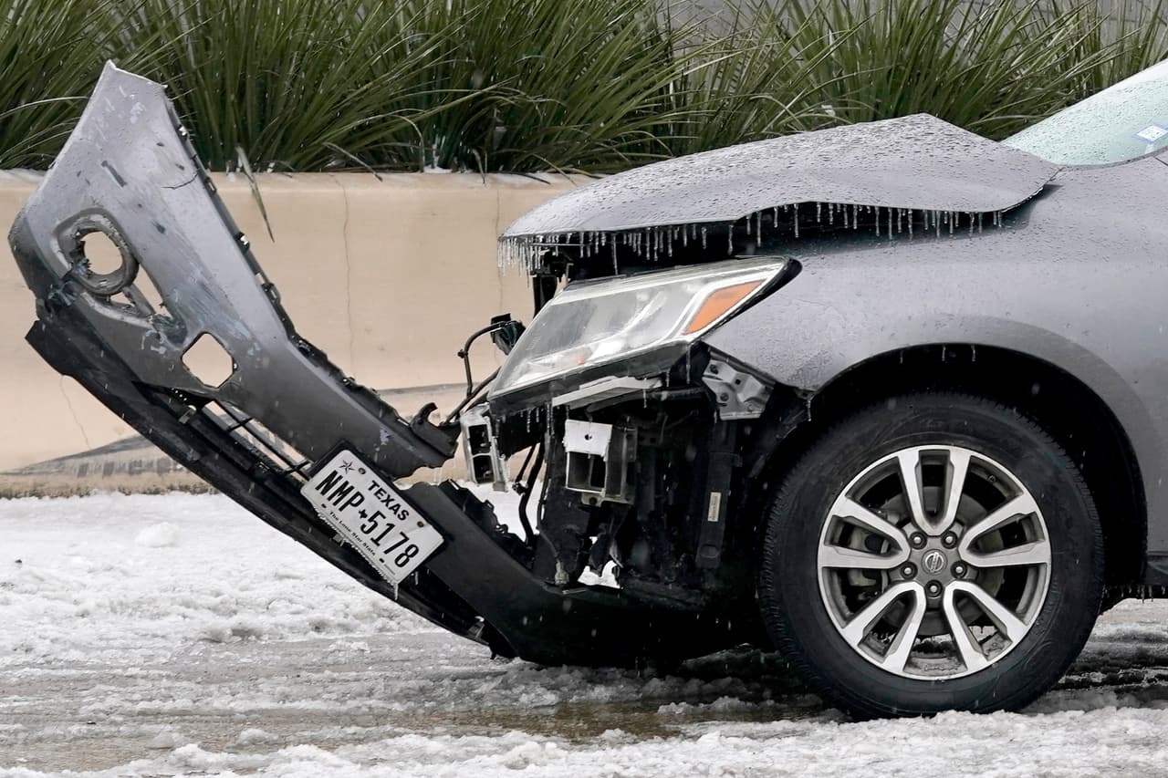 Un auto accidentado con hielo acumulado en la autopista 75, mientras que los trabajadores de emergencia cercanos trabajan para sacarlo de la carretera, el miércoles 1 de febrero de 2023, en Dallas.