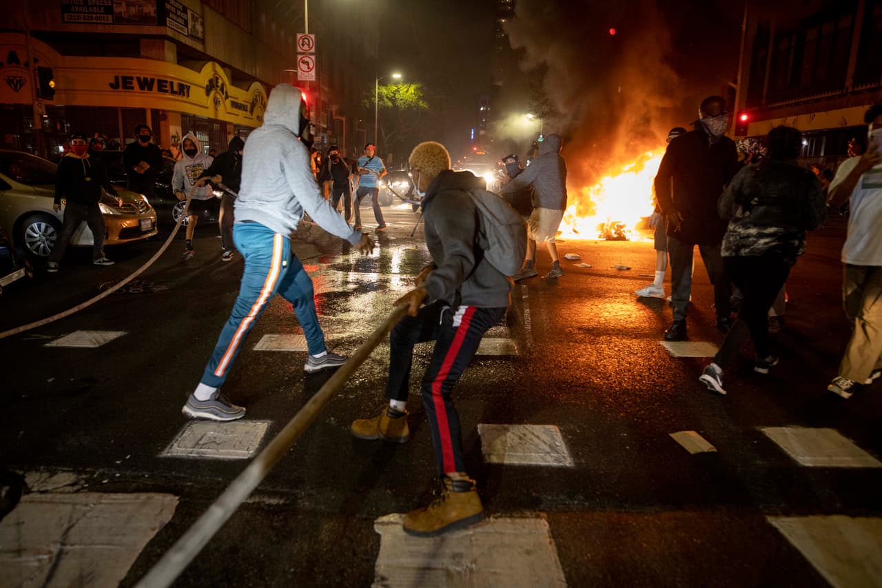Además, botes de basura fueron incendiados. En la imagen los manifestantes le quitan una manguera contra incendios a los bomberos durante una protesta en el centro de Los Ángeles.