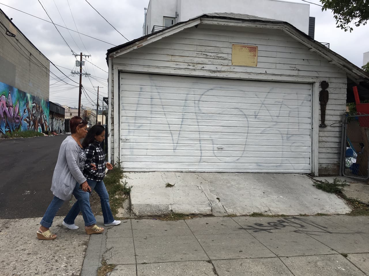 Dos mujeres caminan frente a la cochera de una casa en Hollywood, California, marcada con las siglas de la Mara Salvatrucha.