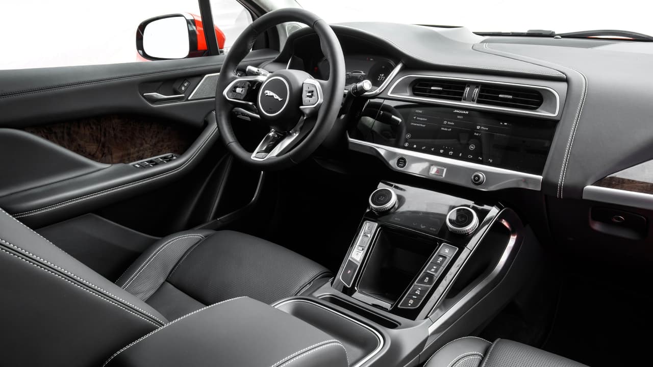 La cabina de la I-Pace tiene un sabor sorprendentemente tradicional para un vehículo eléctrico, acentuado por el hecho de que normalmente los fabricantes de vehículos eléctricos tienden a diferenciarlos visualmente de los autos con motores de combustión interna. El panel de instrumentos, aunque moderno y orientado al conductor retiene la distribución clásica de sus componentes con los instrumentos, es este caso totalmente digitales, frente al conductor.