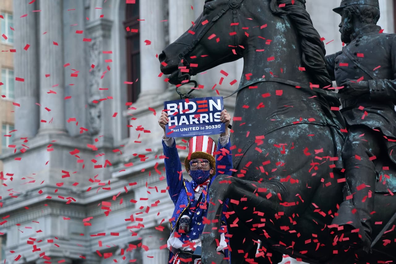 Un hombre vestido como el Tío Sam celebra mientras está parado en una estatua fuera del Ayuntamiento después de que Joe Biden sea declarado próximo presidente. El demócrata Joe Biden ganó la Casa Blanca, dijeron los medios estadounidenses el 7 de noviembre, derrotando a Donald Trump y poniendo fin a una presidencia que convulsionó la política estadounidense, conmocionó al mundo y dejó a Estados Unidos más dividido que en cualquier otro momento en décadas.