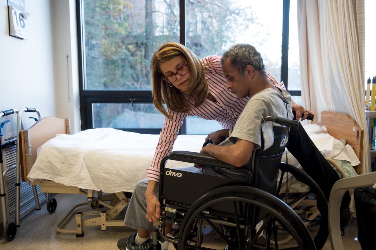 Luz Sanchez helps Gouroa Gomez move from his wheelchair into a bed, which is part of his rehabilitation training. Luz Sanchez demonstrates the rehabilitation techniques she uses in her job at Fort Tryon Center for Rehab & Nursing in New York City, NY, on Novemeber 14, 2017. Gouroa Gomez, who suffered from a stroke six months ago and spent two months in hospital before coming to the Fort Tyron Center, is one of Luz's patients. Photo ©Skyler Reid for Univision Digital