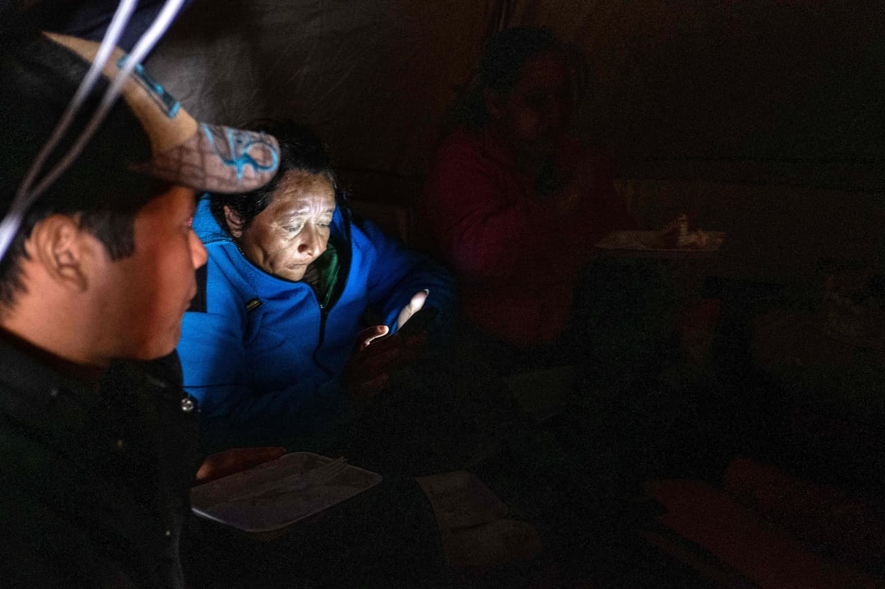 Migrantes centroamericanos de la caravana miran videos en sus celulares y comen durante la víspera del Año Nuevo en un refugio temporal en el centro de Tijuana.