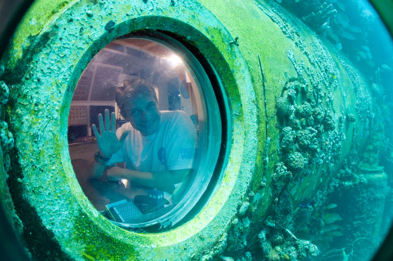 Cousteau saluda a través de una de las ventanillas de Aquarius, que tiene el tamaño de un autobús escolar y aún está en funcionamiento en Cayo Largo, al sur de Florida. 
<br>
<br>Según Forbes, el investigador está recaudando los 135 millones de dólares que harán falta para construir la nueva estación 
<a href="https://www.fabiencousteauolc.org/proteus"><u>Proteus</u></a>, que tendrá alrededor de 370 metros cuadrados, unas diez veces más grande que Aquarius.