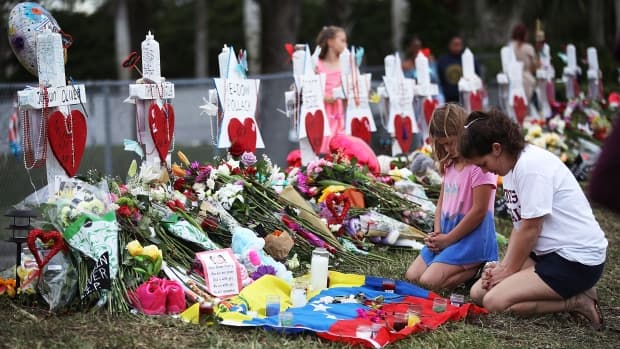 People visit a makeshift memorial setup in front of Marjory Stoneman Douglas High School on Monday in Parkland, Fla. Police have charged a 19-year-old former student for the Feb. 14 shooting that left 17 people dead and wounded others.