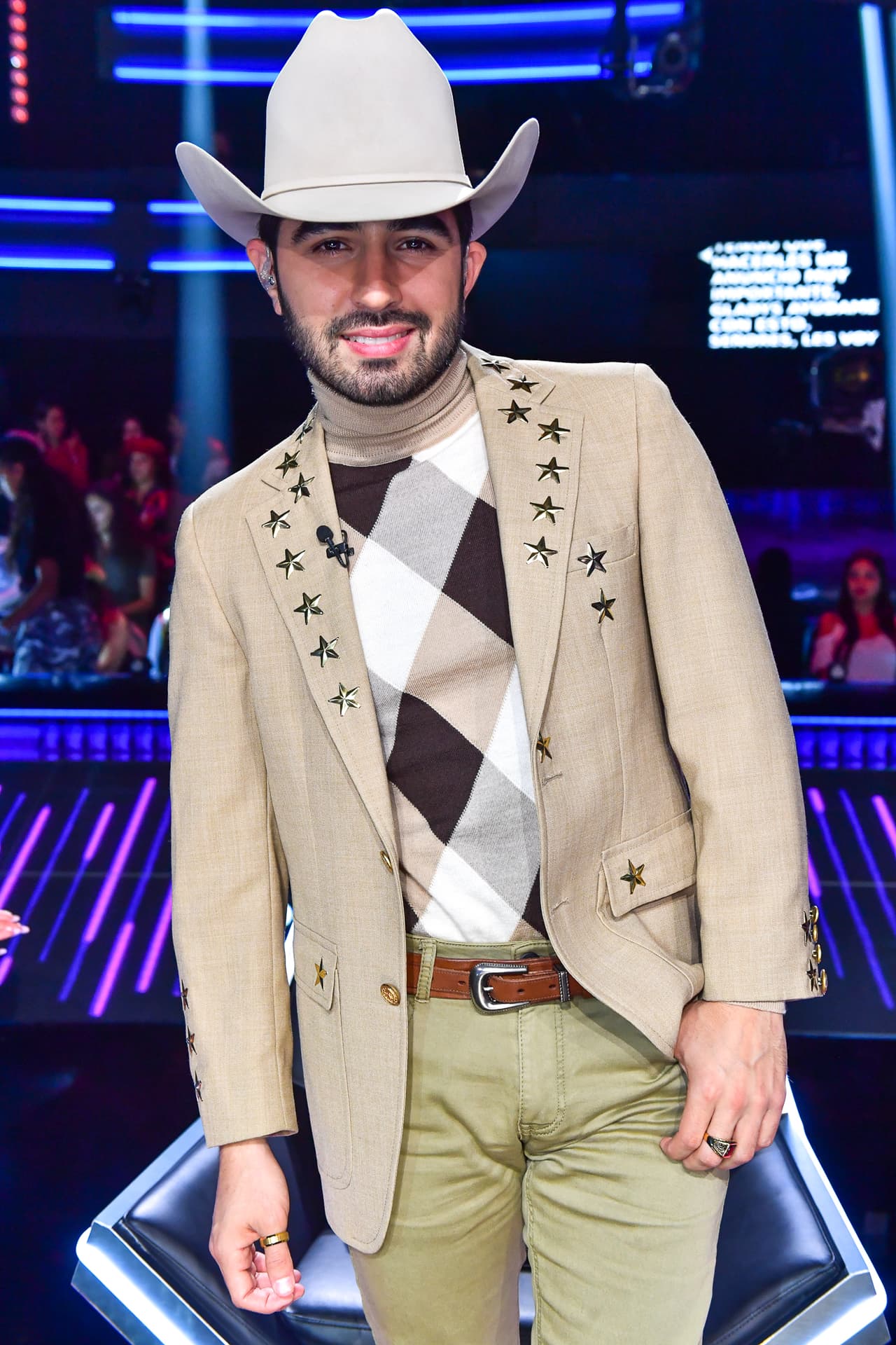Joss Favela sorprendió con esta moderna chaqueta beige con estrellas en las solapas, de la colección de The Storga Project, que combinó con una camisa de cuello de tortuga, pantalones de Dsquared2, botas marrón de Tom Ford y su inseparable sombrero Presidente.