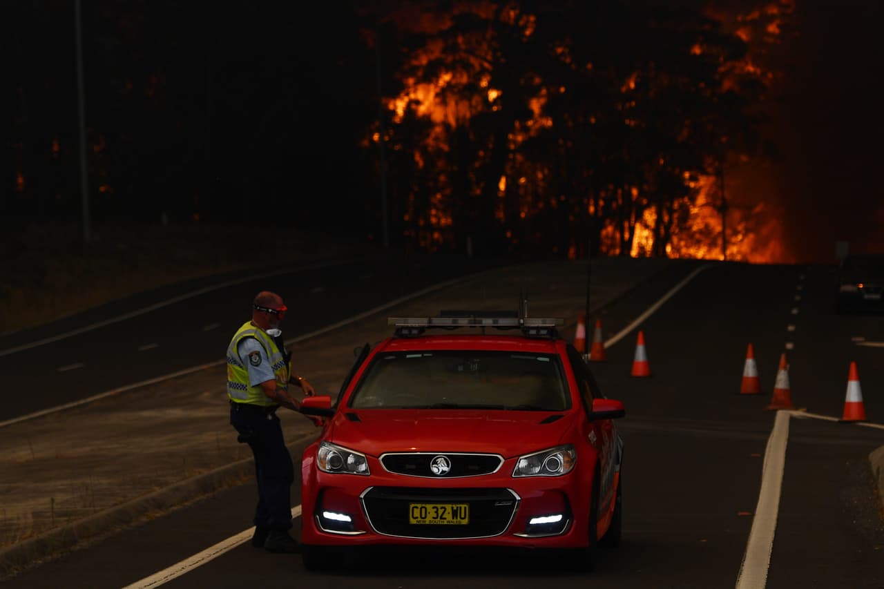 Un policía de Nueva Gales del Sur debe salir en su patrulla tras quedar bloqueada la carretera por las llamas. El lunes, alrededor de 100,000 personas tuvieron que huir de cinco suburbios de Melbourne debido al avance de los incendios.