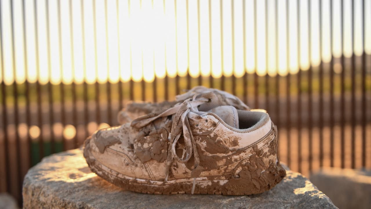 Un par de zapatos con costras de barro quedaron en una piedra cerca de un hueco a lo largo del muro fronterizo entre Estados Unidos y México en Yuma, Arizona.