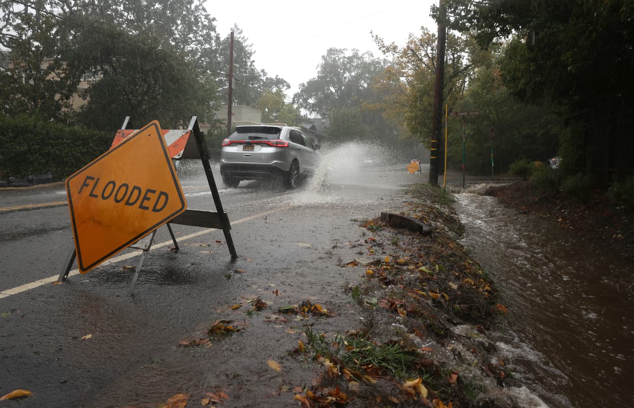 <b>Ross. </b>Un automóvil conduce a lo largo de una calle inundada en Ross, California. El agua corre por un canal que no se dio abasto para desfogar la cantidad de lluvia que cayó.