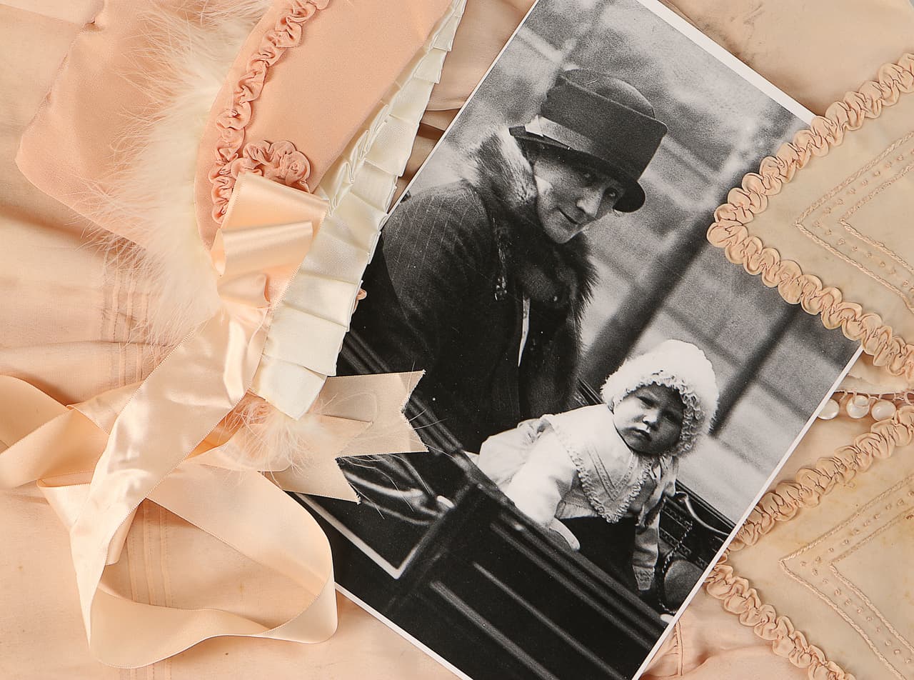 El abrigo de cuello bordado en nudos franceses y bordes satinados será subastado con esta fotografía de una 
<b>pequeña Isabel</b> seriota luciendo el atuendo sentada en
<b> la falda de su niñera</b> Clara Knight.