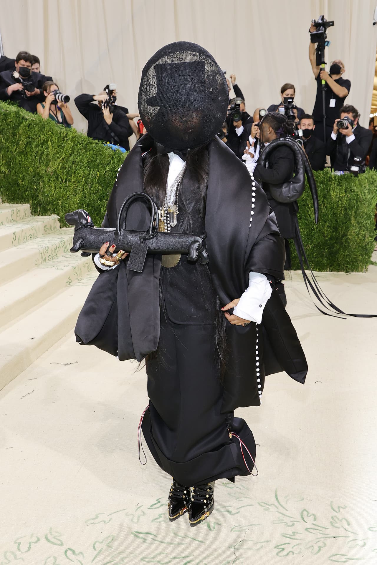 La cantante 
<b>Erykah Badu</b> arribó al recinto con una creación de Thom Browne que de inmediato recibió los flashes de las cámaras. Se trató de un bolso en forma de perro salchicha que complementaba un excéntrico vestuario con prendas maxi en color negro. Entre otros accesorios llamativos usó una máscara de encaje que tapaba su rostro.