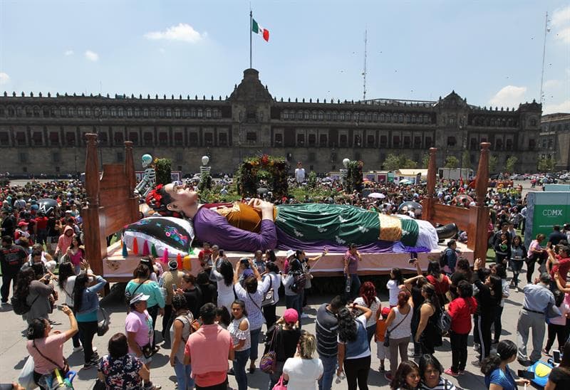En la explanada del Zócalo de la Ciudad de México, inundada con miles de flores, personas vestidas de Frida Kahlo y pinturas inspiradas en la artista mexicana, se exhibe la exposición en honor a la pintora en el 112 aniversario de su natalicio.