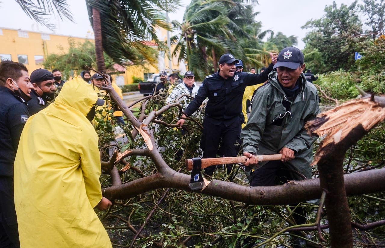 Bomberos retirando árboles caídos en una calle de Cancún. El presidente Andrés Manuel López Obrador ordenó el despliegue de más de 5,000 efectivos de las fuerzas armadas y personal de emergencia para colaborar en las tareas que fueran necesarias.