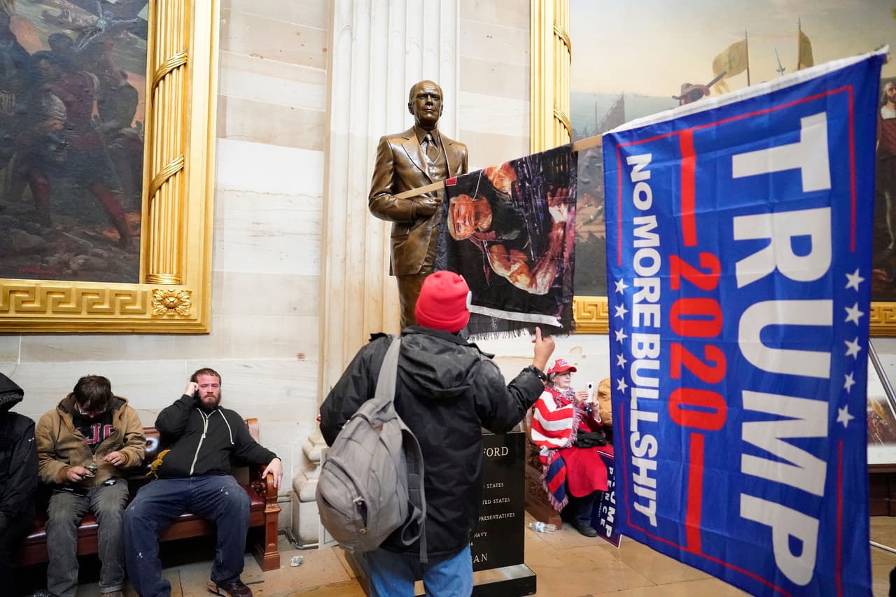 <b>Piezas de arte históricas perturbadas por la turba</b>
<br>
<br>Una bandera de la campaña de Trump fue encajada en una escultura de Henry Ford que está en la Rotonda del Capitolio. Esta fue una de las piezas que fue manipulada por los asaltantes y sirvió de escenario para las fotografías y videos que se tomaron.
<br>