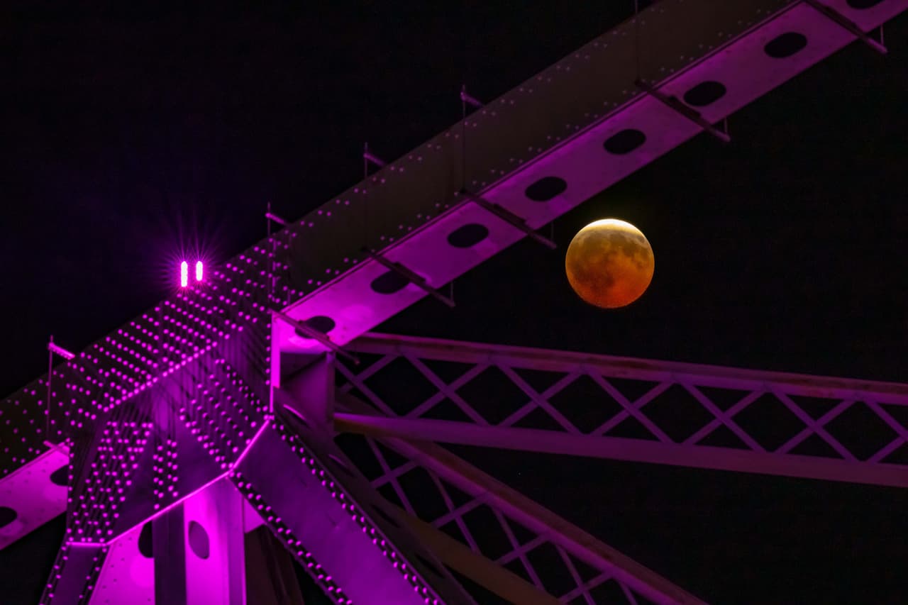 Un eclipse lunar parcial, visto a través de las vigas de acero -iluminadas de color morado- de Crescent City Connection, un par de puentes que cruzan el río Mississippi, en Nueva Orleans, el 27 de agosto de 2026.