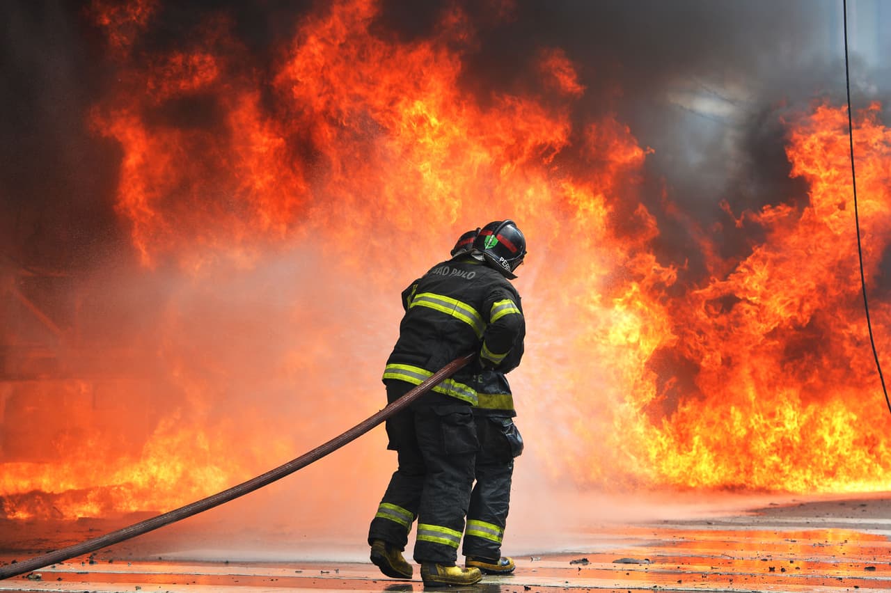 Firefighters try to extinguish the fire on a bus set ablaze during clashes between the Riot Police and members of the Homeless Workers' Movement (MTST) during the eviction of an abandoned hotel in downtown Sao Paulo, Brazil, on September 15, 2014. Some 200 families were living in the building. AFP PHOTO / NELSON ALMEIDA (Photo credit should read NELSON ALMEIDA/AFP/Getty Images)