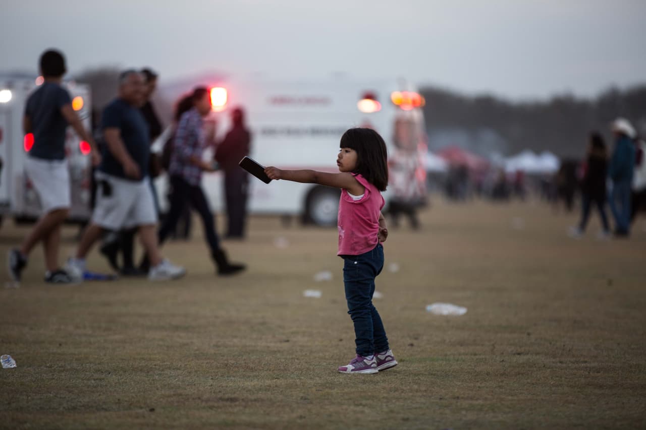 Una niña de corta edad señala a su papá con la mano en la que lleva un Smartphone.
