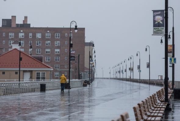 Un hombre camina por el paseo marítimo, mientras se observa el clima lluvioso en Long Beach.