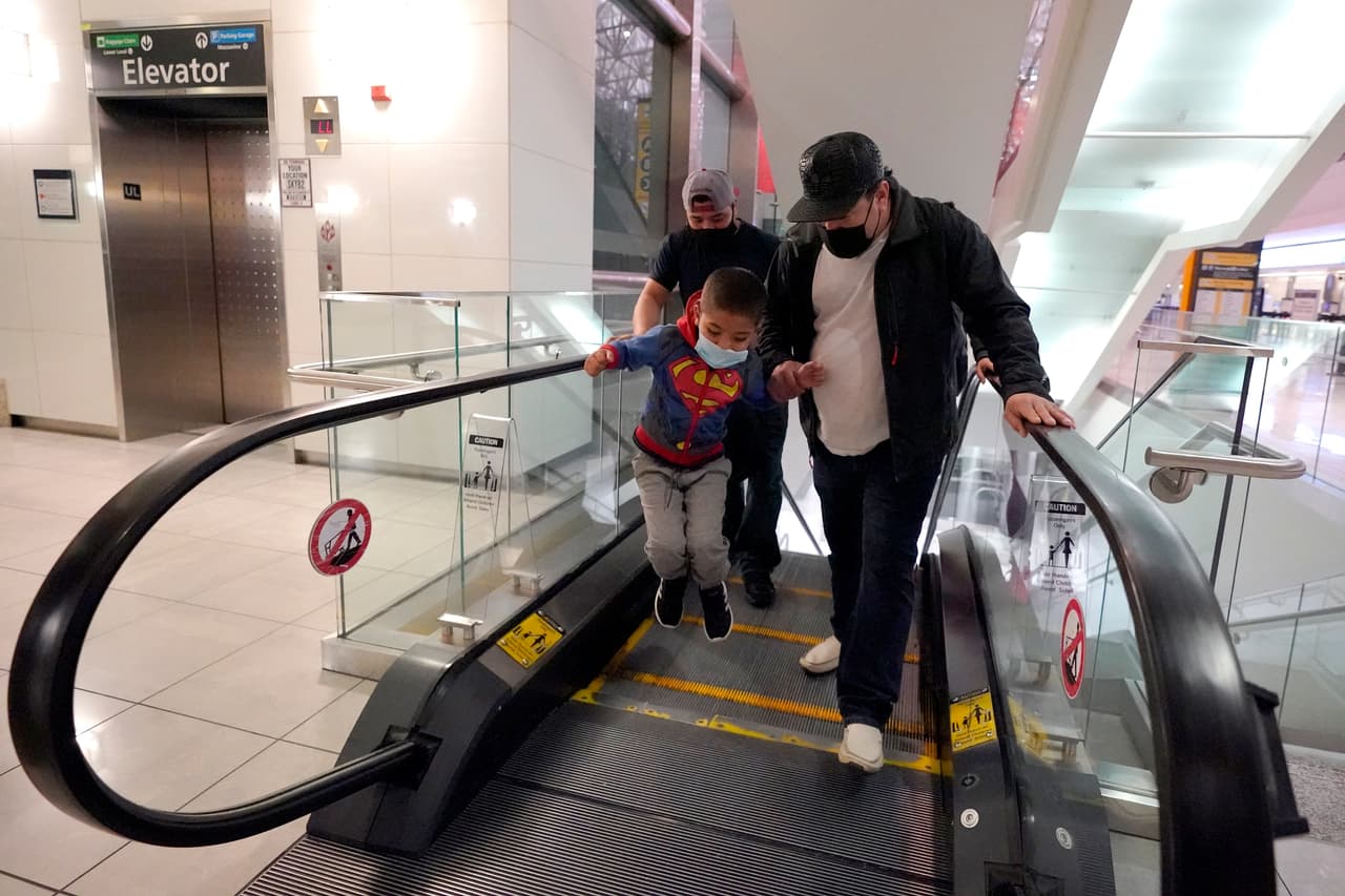 Yancarlos salta en una escalera mecánica mientras sostiene la mano de un amigo de su familia, Dimas Barahona, en el Aeropuerto Internacional Thurgood Marshall de Baltimore-Washington, en Linthicum, Maryland. “No había visto yo esto”, dijo mientras se agachaba para poner sus manos sobre la superficie móvil.