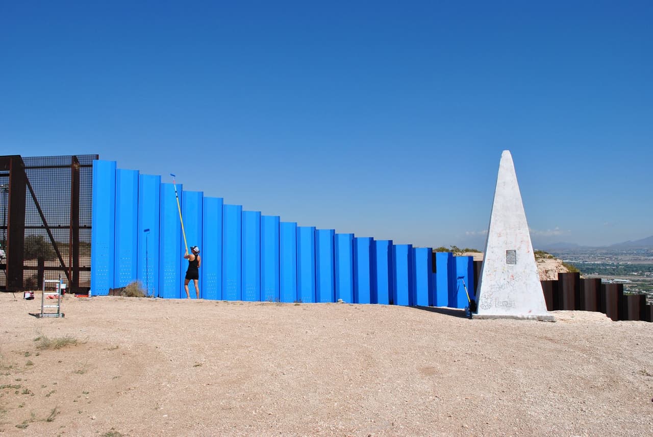 Ana Teresa Fernández, a Mexican artist, paints the border fence located between Sunland Park, New Mexico and Ciudad Juárez, Mexico. The painting creates an optical illusion, making this stretch of fence appear to merge with the sky.