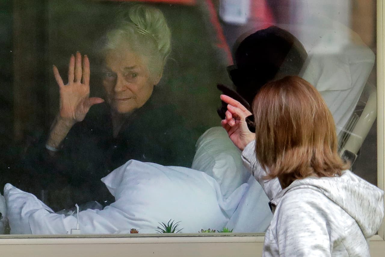 <b>Marzo 11. La pandemia golpea el estado de Washington.</b> Judie Shape saluda a su hija Spencer a través de una ventana de un centro de salud en Seattle. El estado de Washington fue el primero en sentir los efectos de la pandemia, que afectó especialmente a las residencias de presonas mayores. 
<br>Ese mismo día la organización mundial de la salud declaró oficialmente al covid-19 como una pandemia. 
<br>